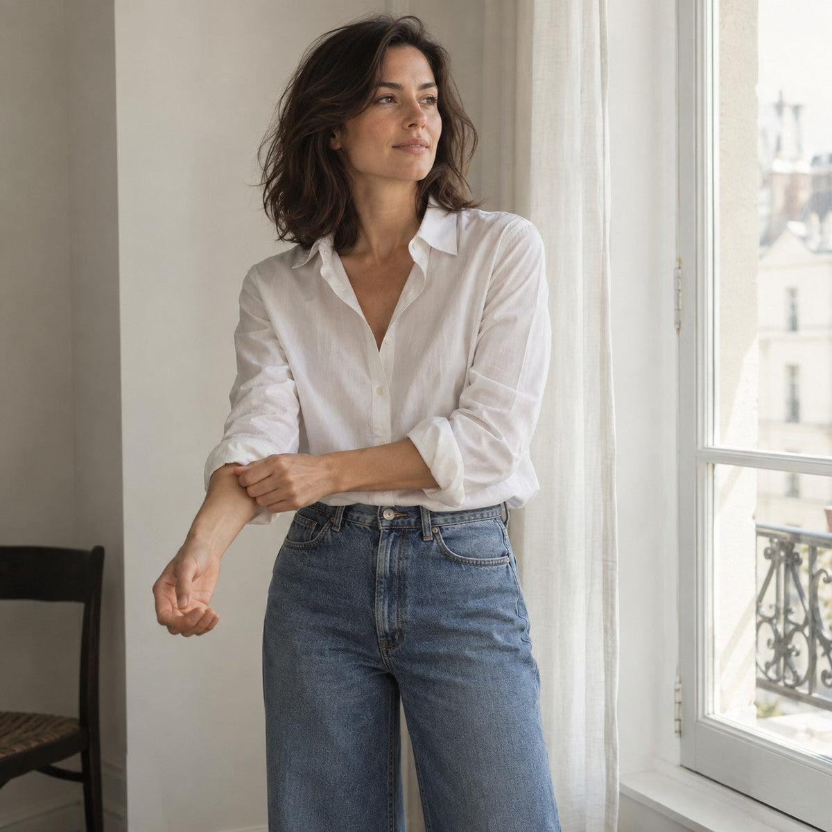 Woman in a white shirt and vintage blue denim beside a sunlit window.